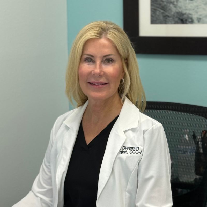 Dr. Jill Diesman, audiologist, smiling in a white lab coat over black scrubs